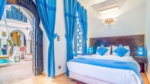 A bedroom with a large bed, blue curtains, a wooden headboard, and a view of an outdoor area with a pool. - Riad Aliya (Marrakech)