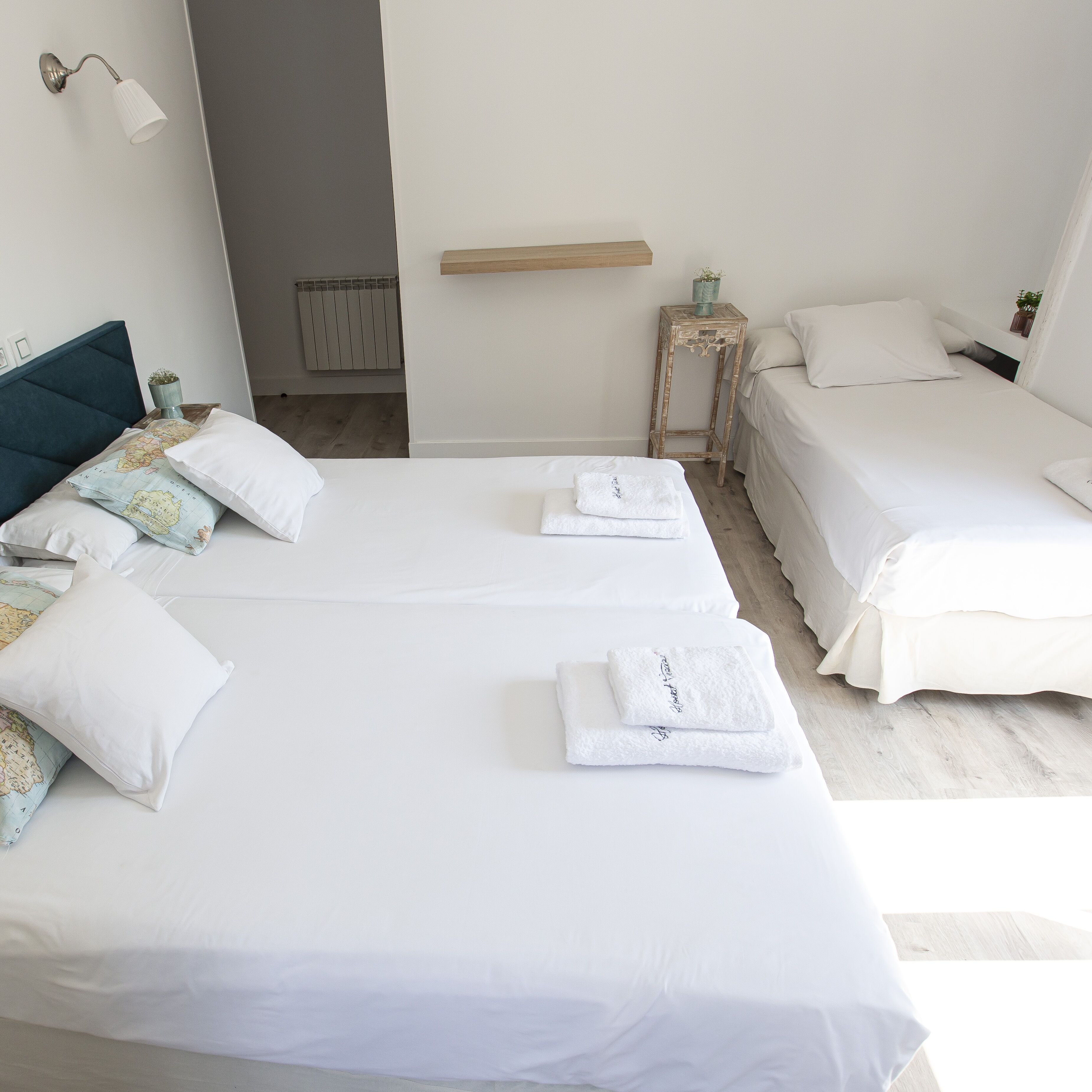 A hotel room with two beds, white bedding, a map pillow, a small table with a plant, and a radiator.
