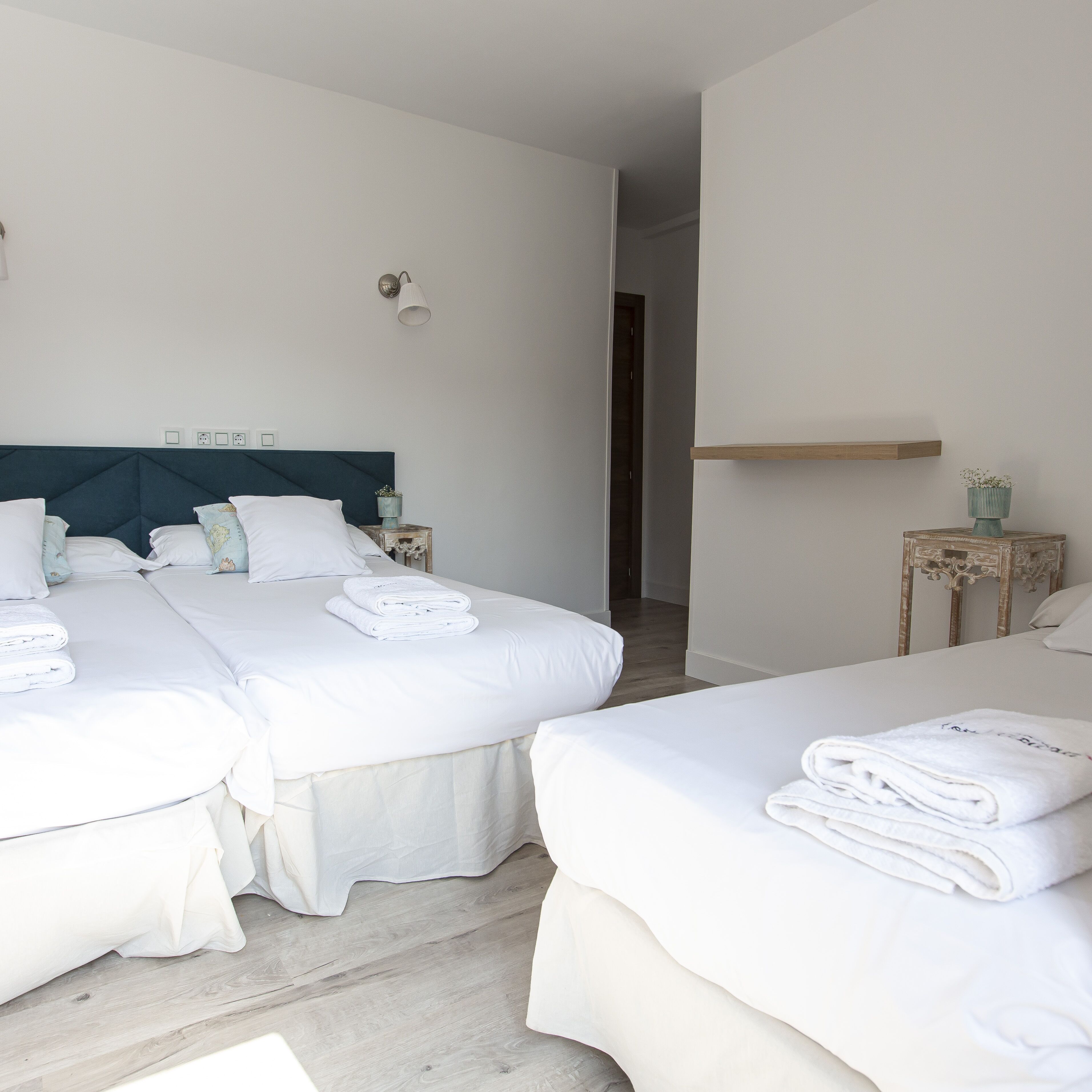 A hotel room with two beds, a wooden headboard, a bedside table with a lamp, and a small plant on a side table.