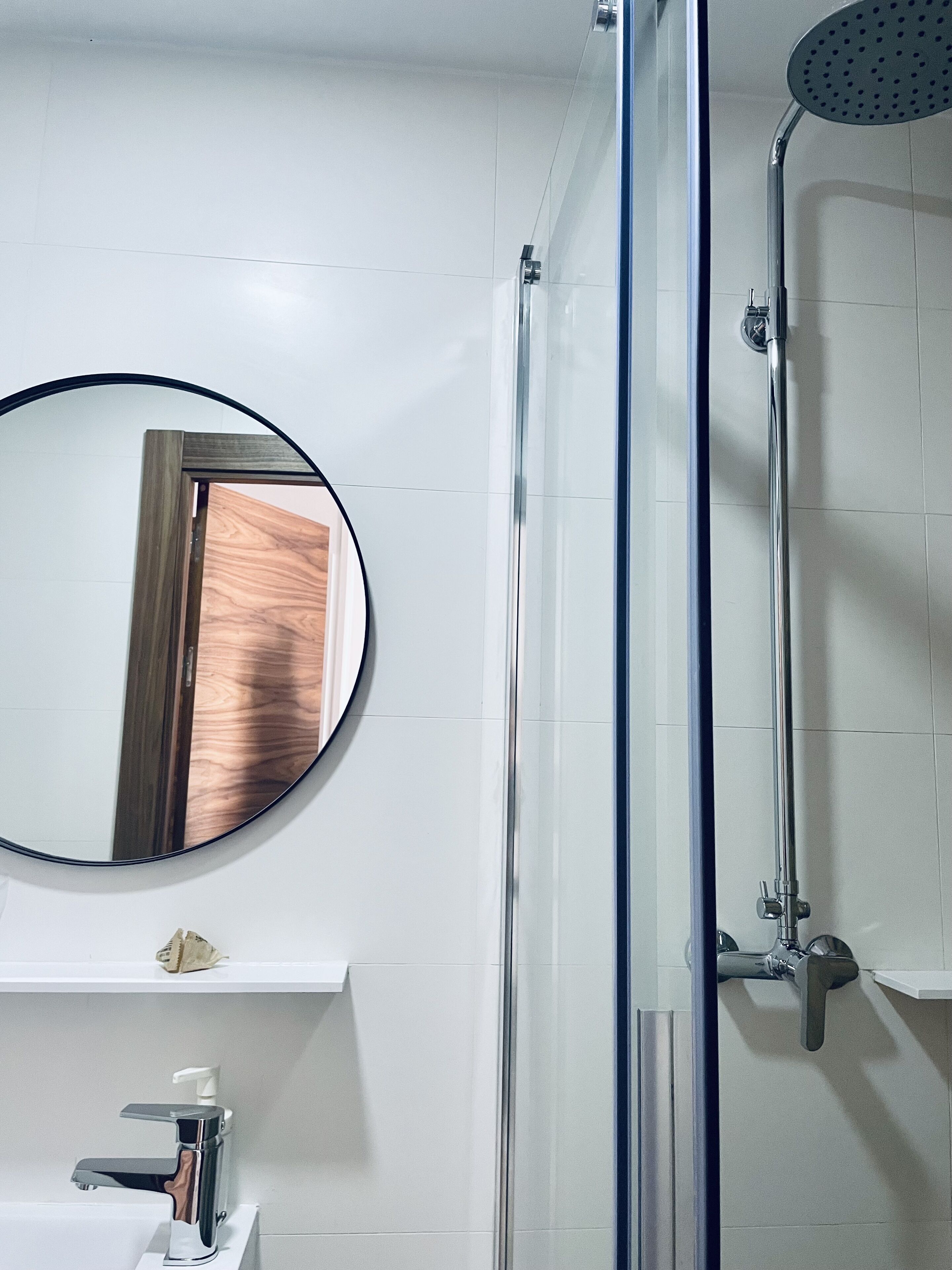 A bathroom with a glass-enclosed shower, a round mirror, and a white sink with a faucet.