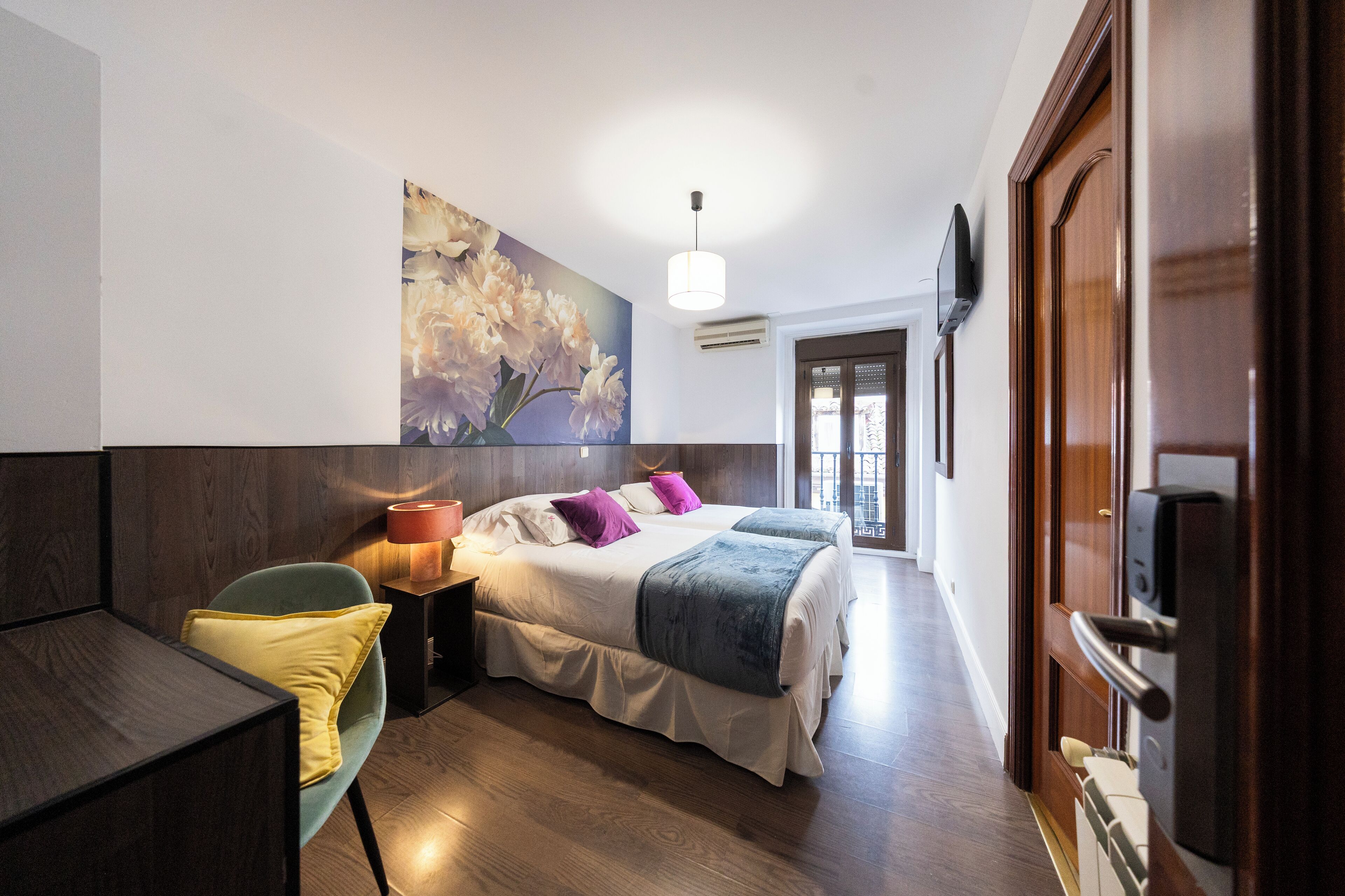 A bedroom with a bed, bedside table, chair, and a wall-mounted TV.