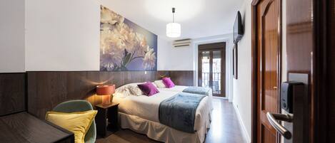 A bedroom with a bed, bedside table, chair, and a wall-mounted TV.