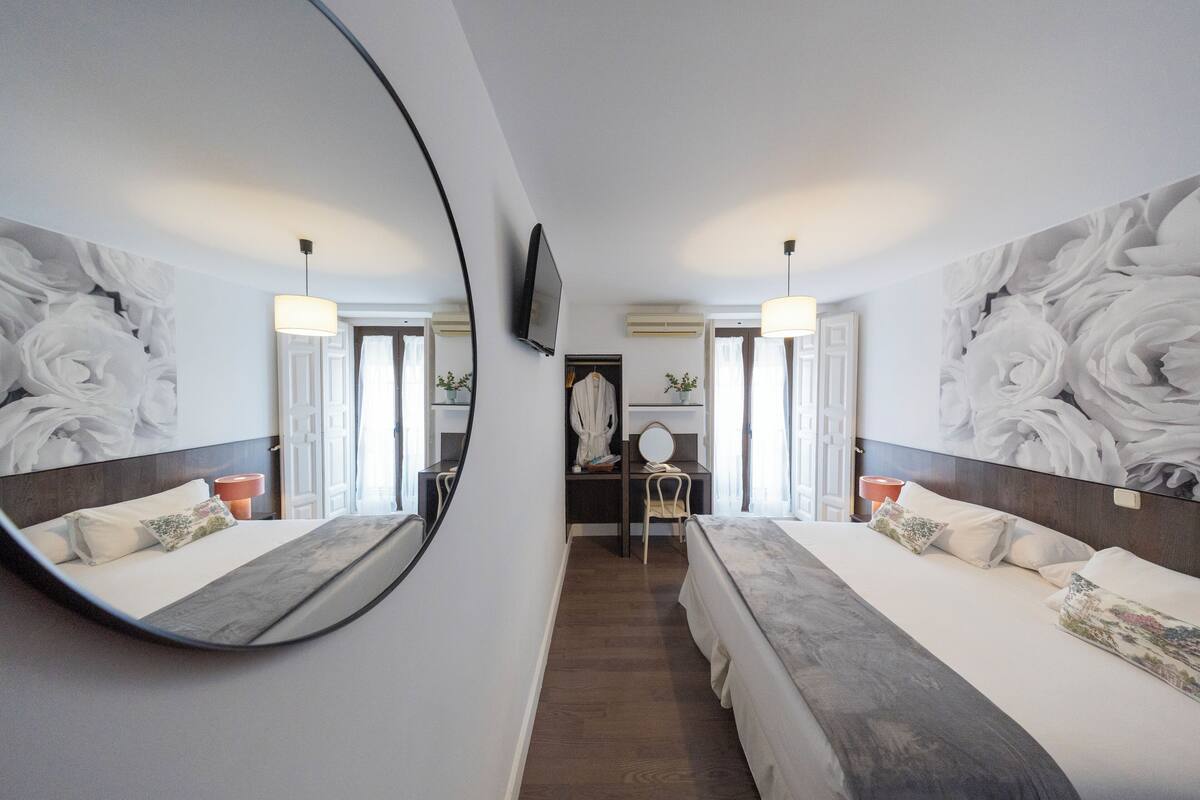 A hotel room with two beds, a large mirror, a TV, and a desk with a chair.