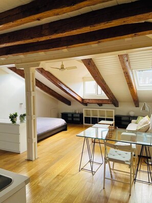 Un dormitorio en el ático con vigas de madera a la vista, una cama, una mesa de comedor de vidrio y un ventilador de techo.