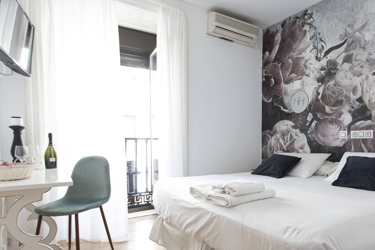 A hotel room with a bed, a desk, a chair, and a balcony with a view.