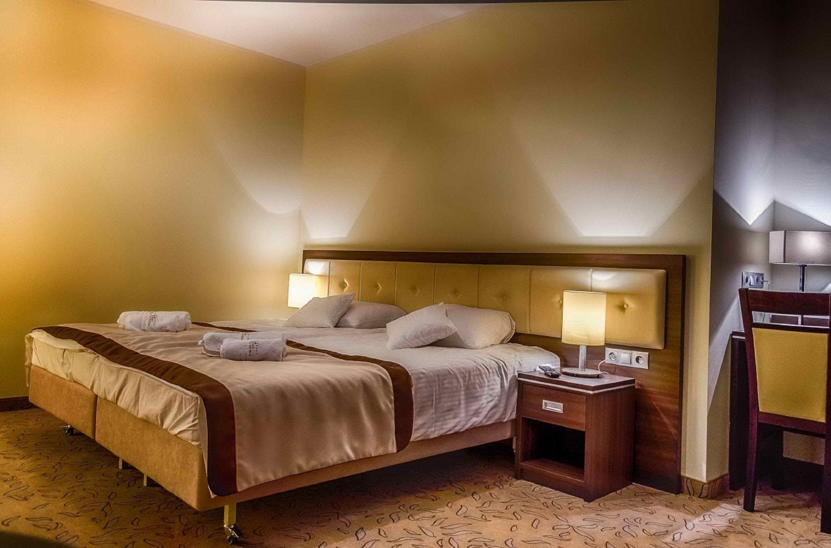 A hotel room with a large bed, bedside lamps, a wooden nightstand, and a chair.