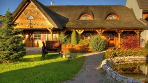 A wooden building with a thatched roof, a sign reading "OBERI 4 POD STRZECHA", and a stone pathway leading to a pond. - Hotel Czardasz Spa & Wellness (Plock)