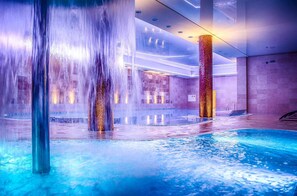 Una piscina interior con múltiples chorros de agua y un interior moderno y bien iluminado.
