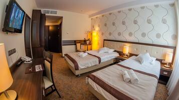 Habitación de hotel con dos camas, un escritorio, una silla, un televisor y la puerta del baño.