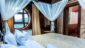 A bedroom with a bed, white curtains, a window with a view of mountains, and a wooden door. - Predeal Comfort Suites (Predeal)