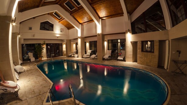 A large indoor swimming pool with multiple lounge chairs and a ceiling with skylights. - Predeal Comfort Suites (Predeal)