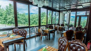 A restaurant with large windows offering a view of a mountainous landscape. Tables are set with brown leather chairs and orange checkered tablecloths. - Predeal Comfort Suites (Predeal)