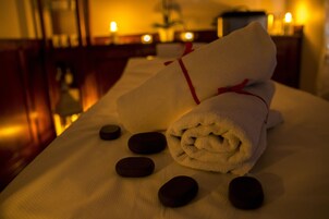 A neatly arranged massage table with a rolled towel and a red ribbon, surrounded by smooth stones.