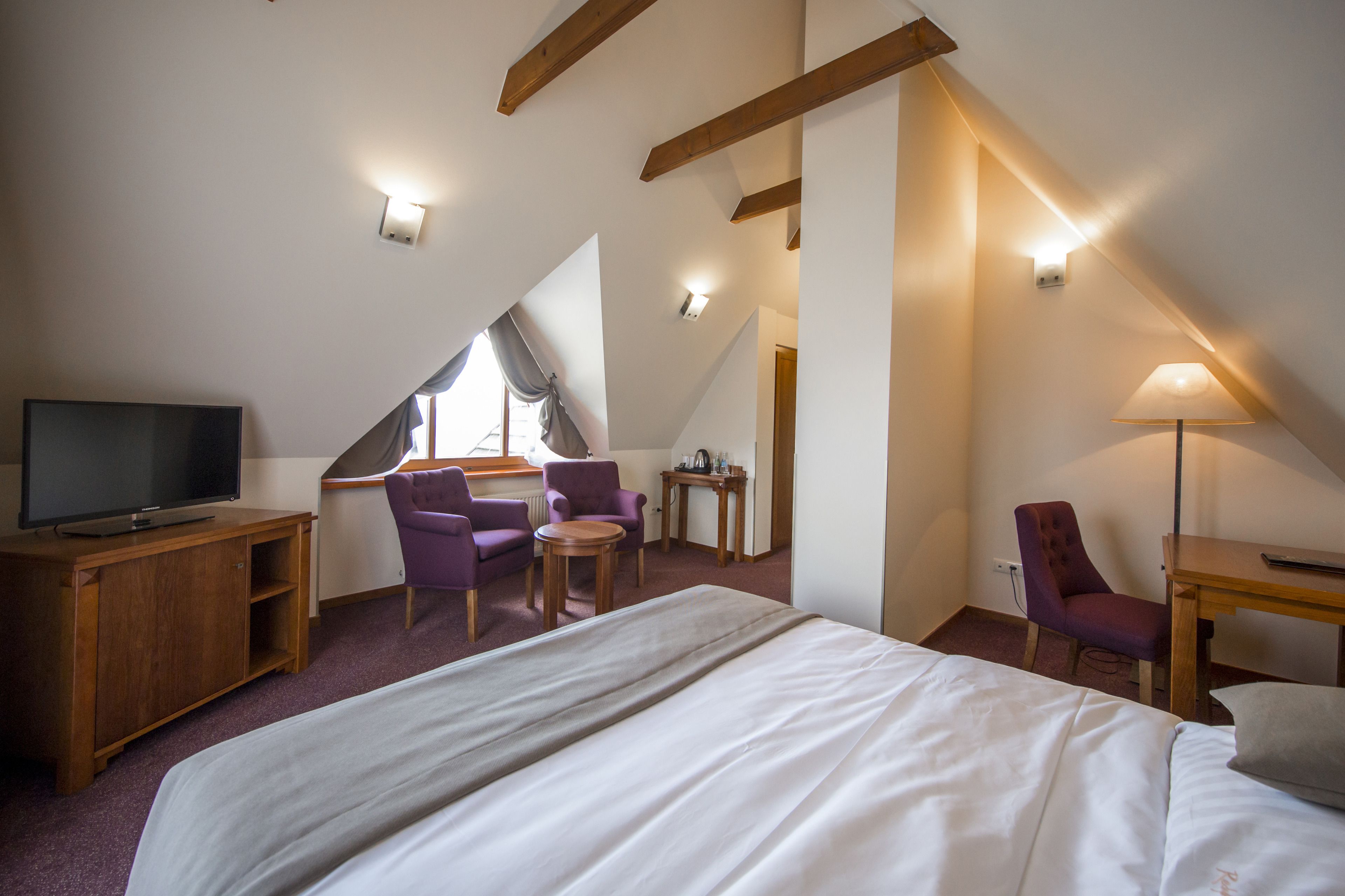 A hotel room with a bed, a TV, a desk, and two chairs.