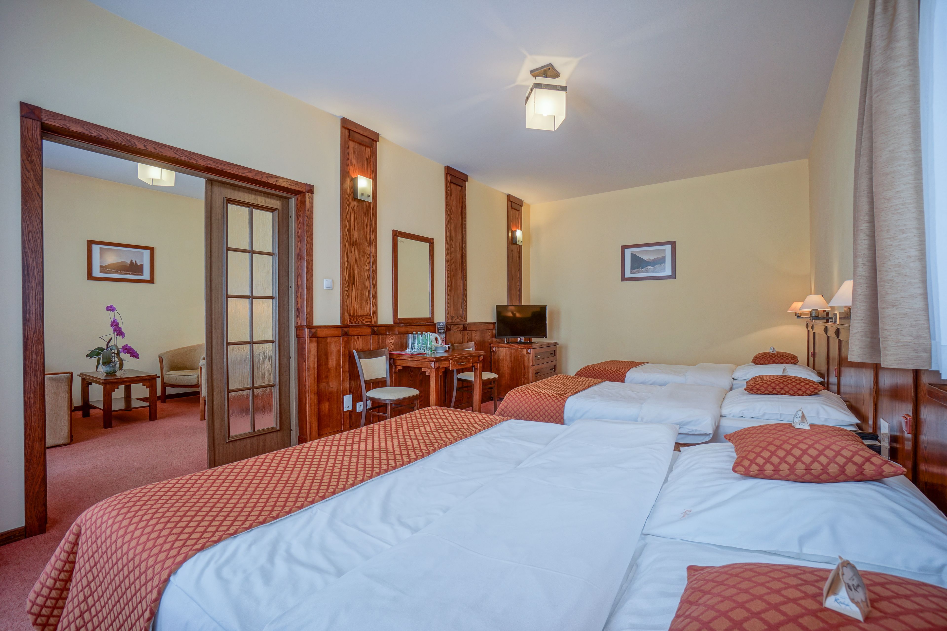 Een hotelkamer met drie bedden, een bureau met een stoel, een televisie en een kleine tafel met een bloevas.
