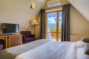 A hotel room with a bed, a TV, a chair, a lamp, and a view of mountains through a large window.