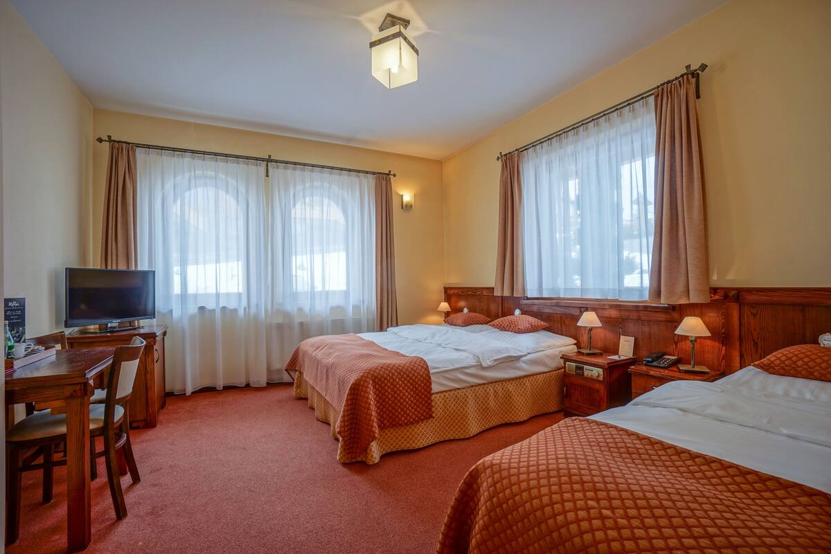 A hotel room with two beds, a desk with a television, and a dining area.