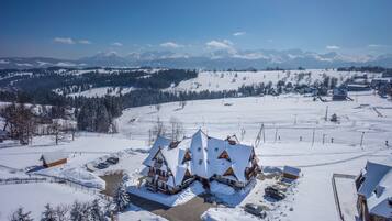 A snow-covered lodge with multiple buildings, a ski slope, and a mountainous backdrop.