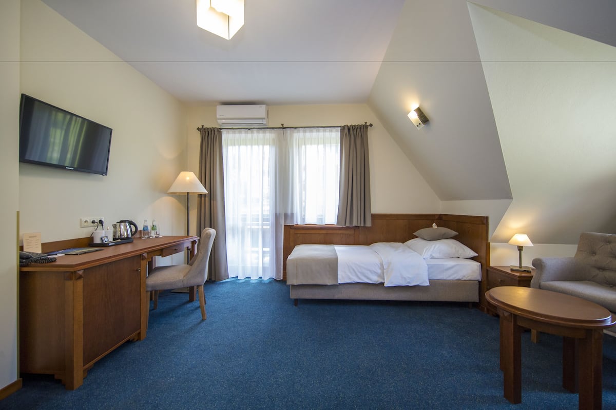 A hotel room with a bed, desk, chair, TV, and a small table.