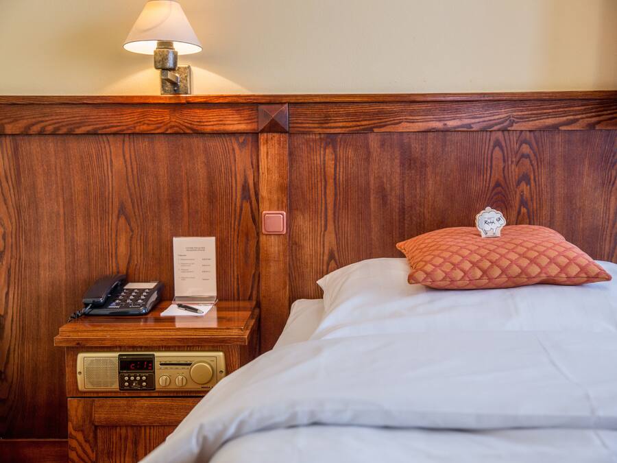 A wooden headboard with a lamp, a bedside table with a phone, a radio, and a pillow.