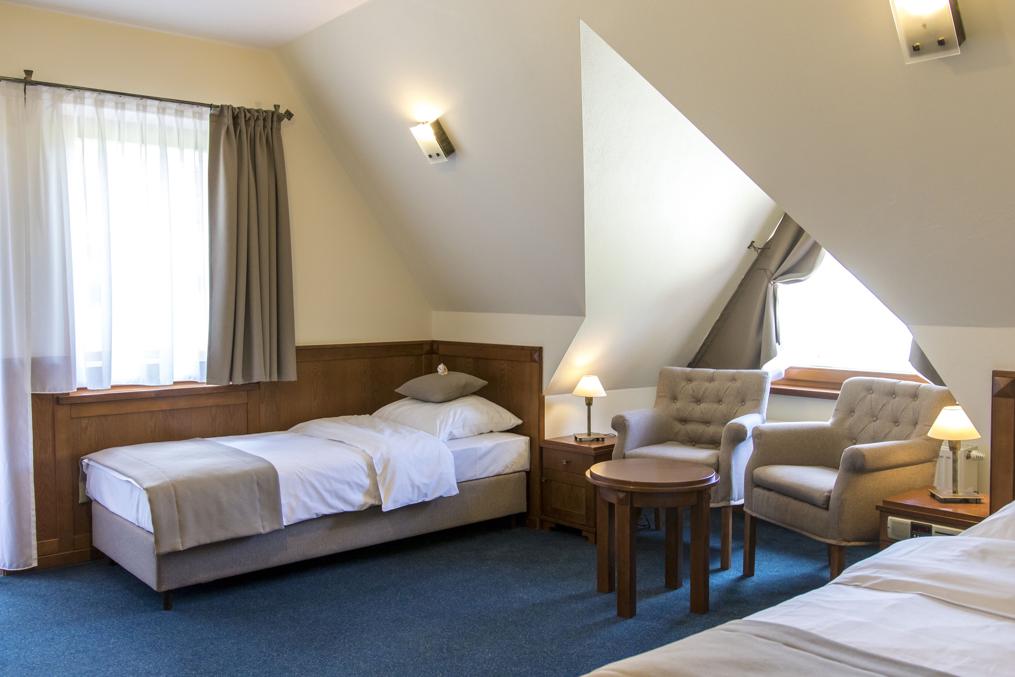 A hotel room with a bed, two armchairs, a small table, and a nightstand with a lamp.