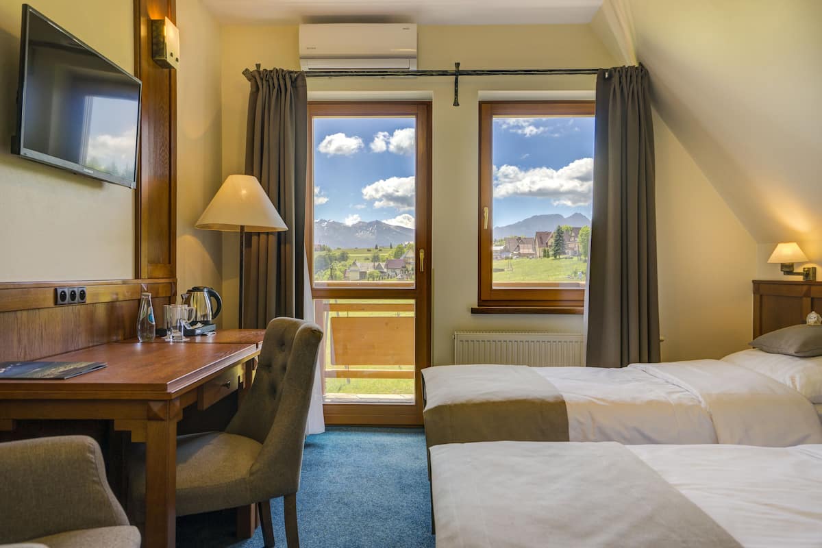 A hotel room with a bed, a desk with a chair, a TV, and a view of mountains through the windows.