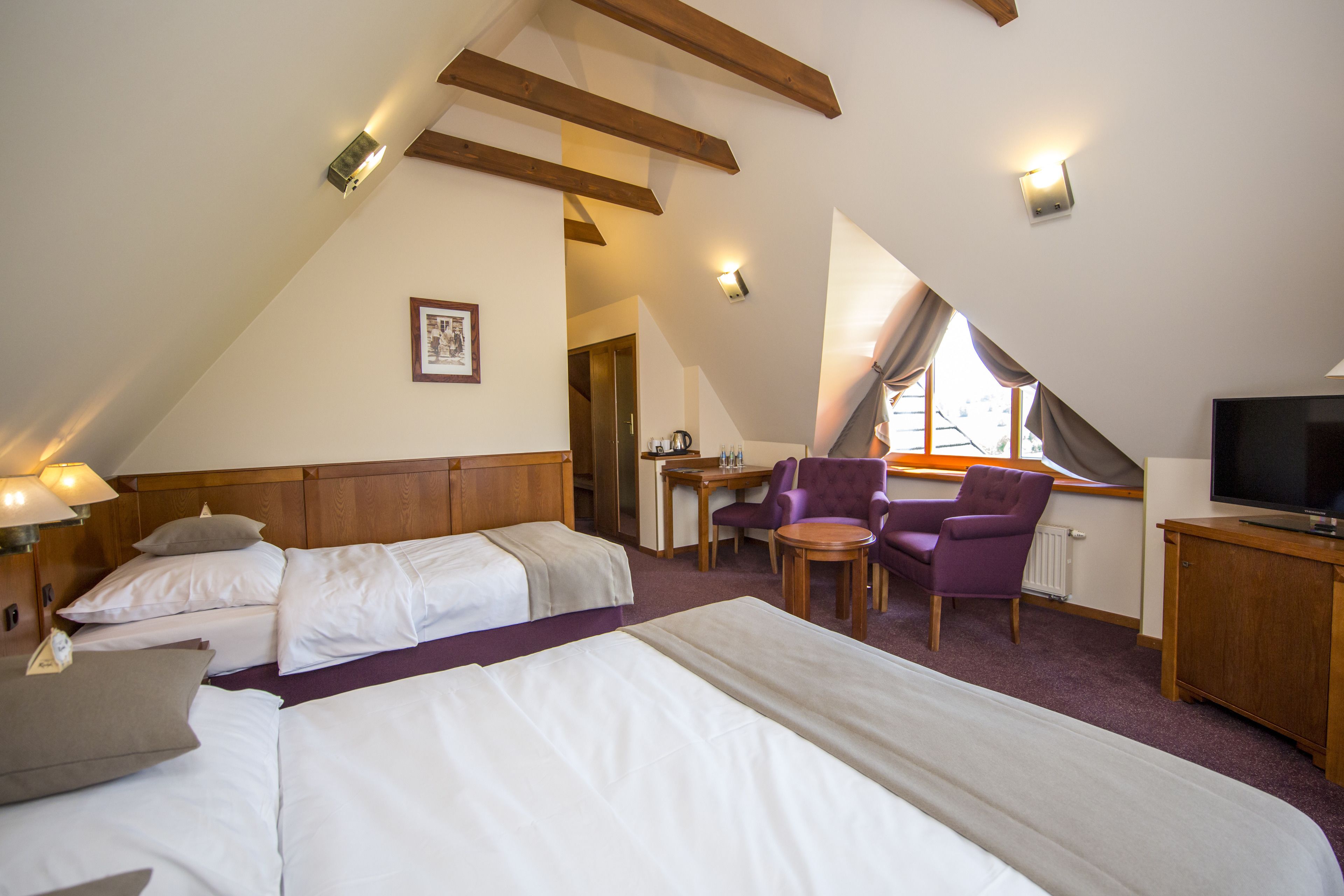 A hotel room with two beds, a desk, a chair, a television, and a window with curtains.