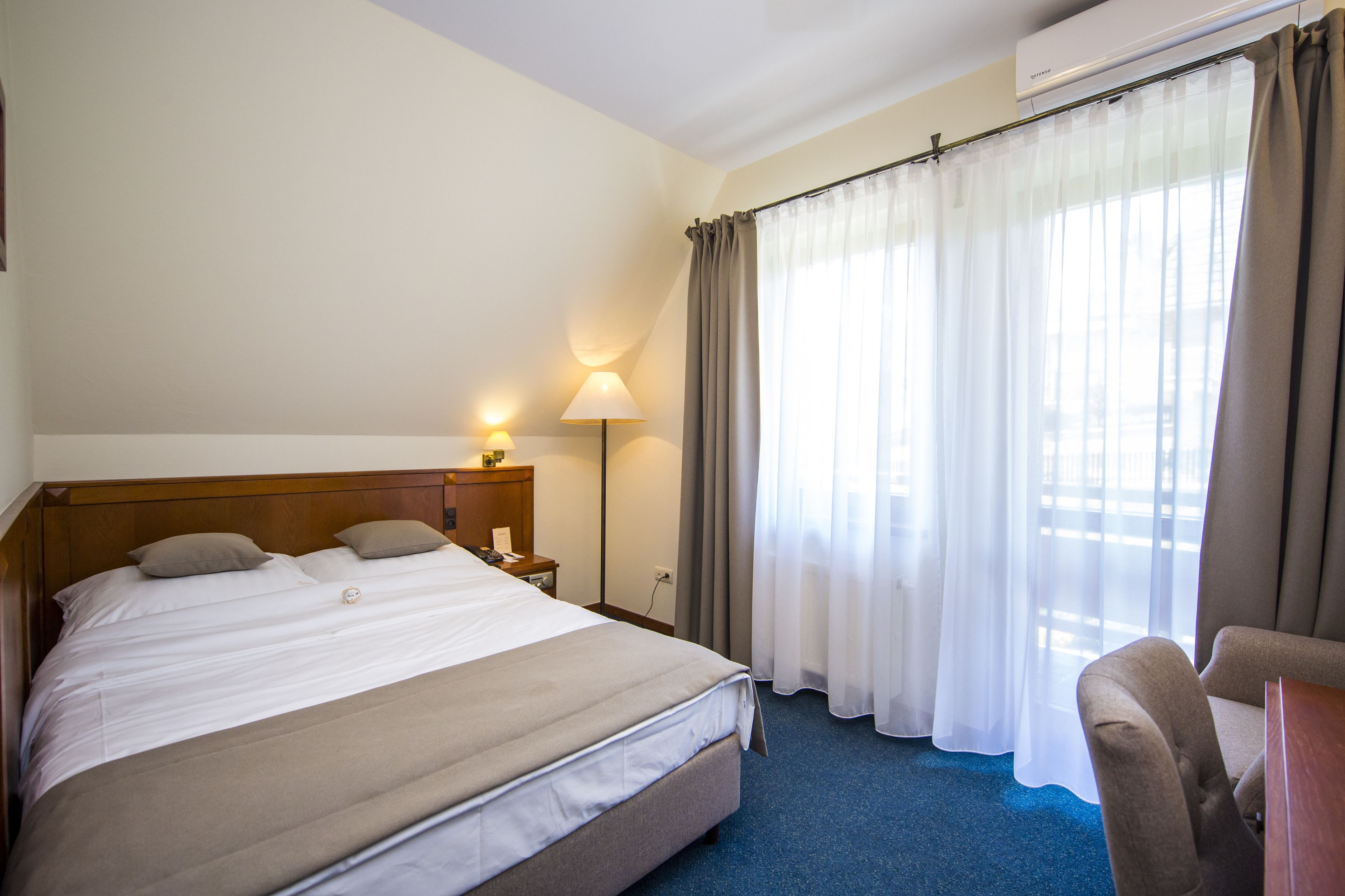 Une chambre d’hôtel avec un grand lit, une table de chevet avec une lampe, une chaise et une fenêtre avec des rideaux.