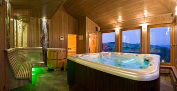 A wooden spa room with a hot tub, a bench, and large windows offering a view of the countryside.