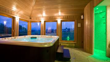Una cabaña de madera con jacuzzi, ventanas amplias y un área de ducha iluminada de verde.