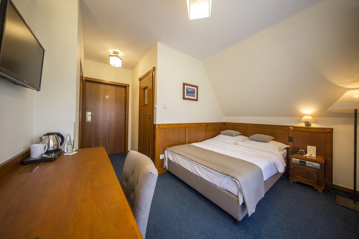 A hotel room with a bed, bedside table, chair, desk, and a television.