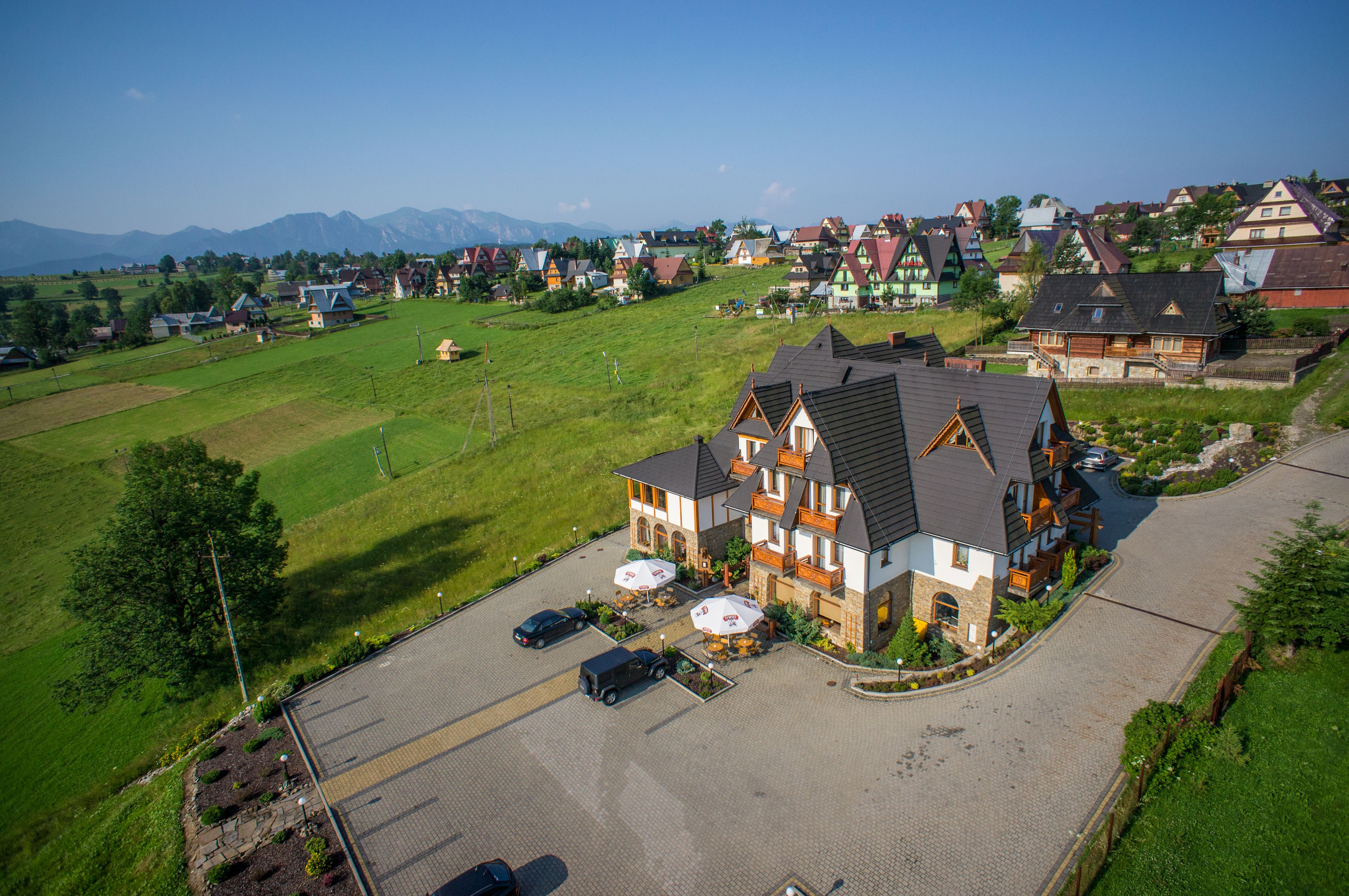 A large, multi-story house with a paved driveway and a parking area.