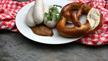 A plate with sausages, a pretzel, and a sauce on a wooden table with a red and white checkered cloth.