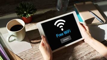 En tablet viser en skærm med "Free WiFi" og en "Connect"-knap, holdt af en person.