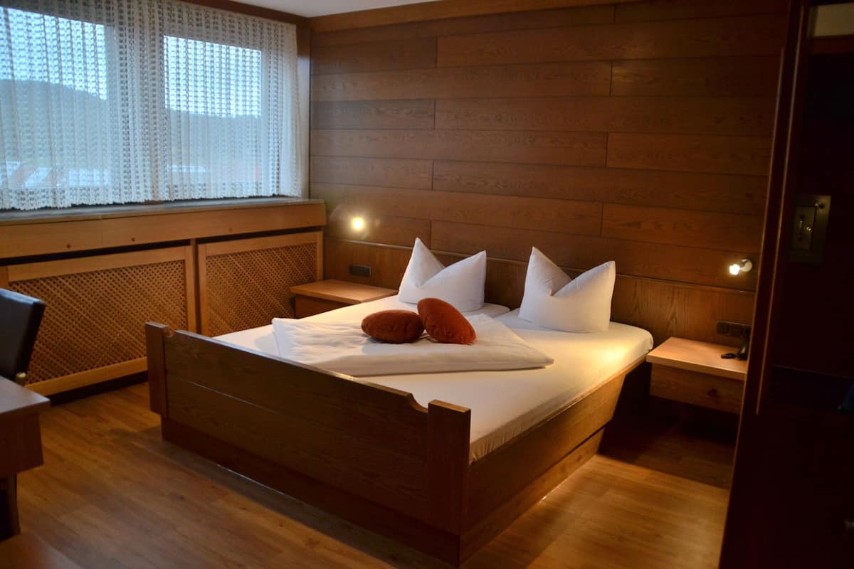 A wooden bed with white bedding, two pillows, and a bedside table with a lamp.