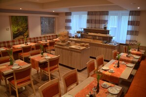 Un restaurante con varias mesas y cabinas, una zona de bar central y una cocina al fondo.