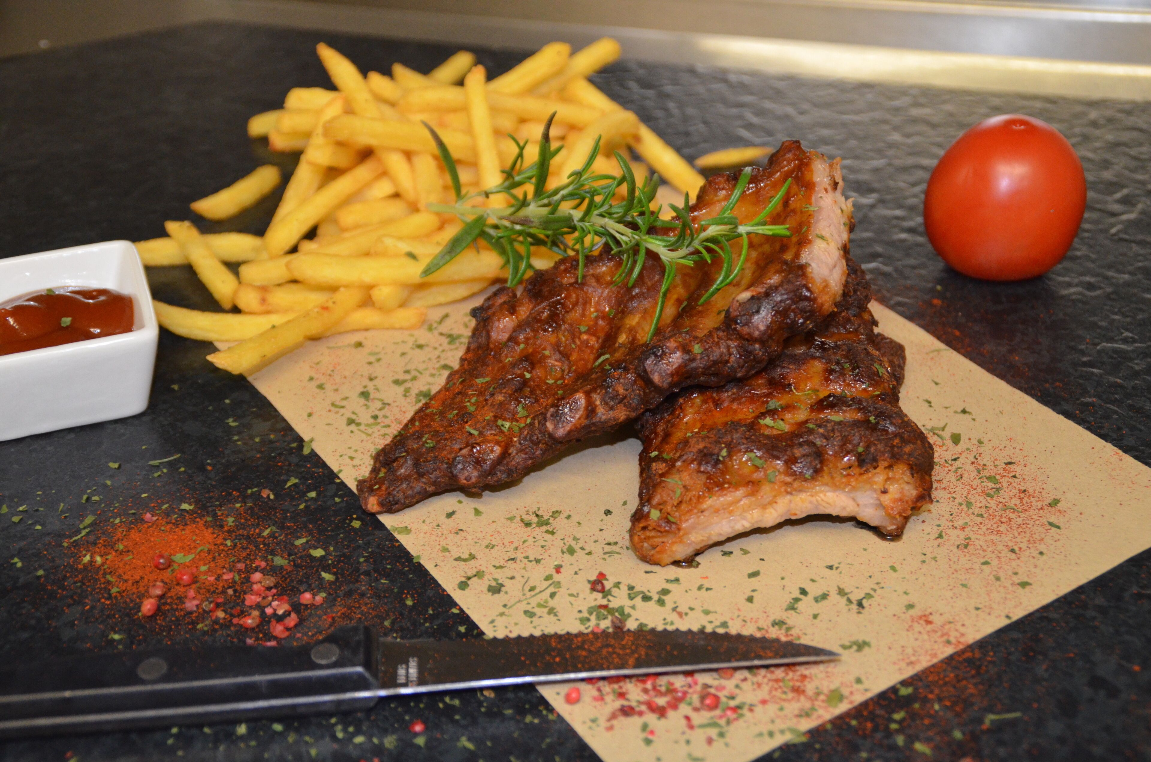 A plate of ribs with fries and a tomato on a cutting board.