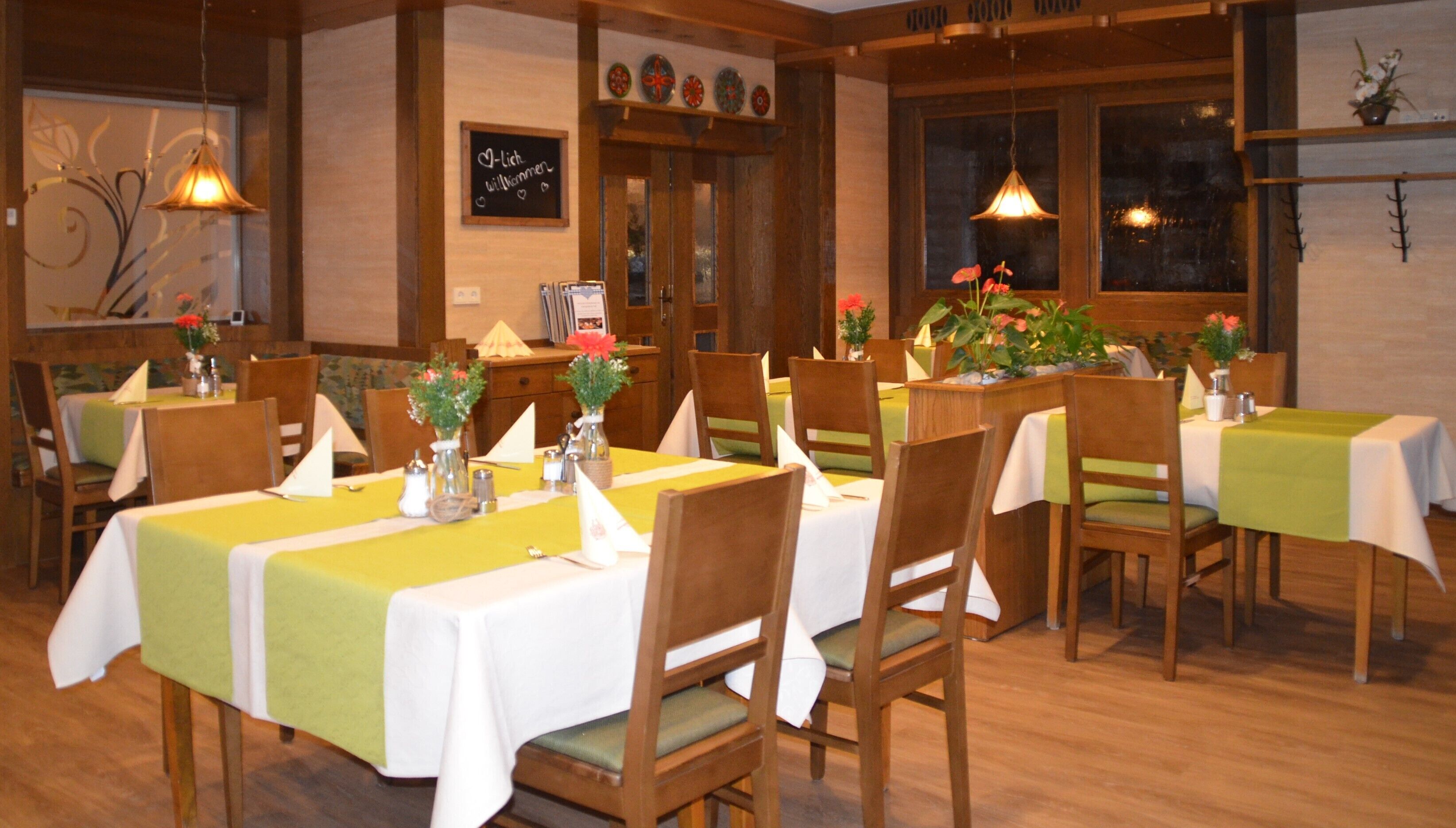 Un restaurante con mesas y sillas de madera, cada conjunto con manteles blancos y servilletas verdes.