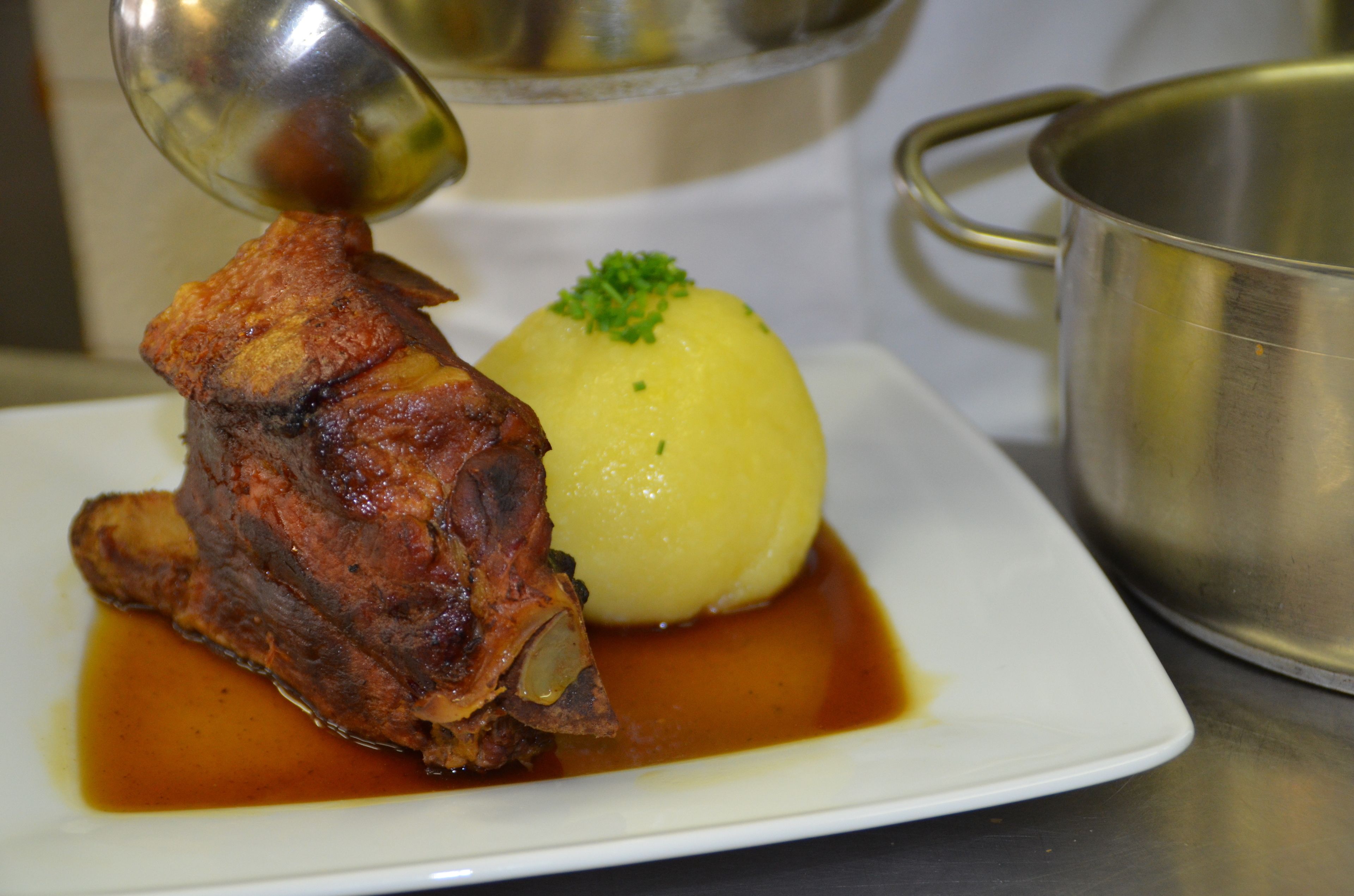 A plate with a roasted meat and a boiled potato garnished with herbs.