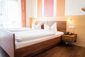 Cama doble con cabecera de madera, mesita de noche con teléfono y toma de corriente.