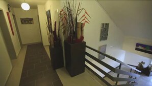 A staircase with a handrail, a potted plant, and a wall-mounted light fixture. - Art Inn Hotel Dinslaken (Dinslaken)