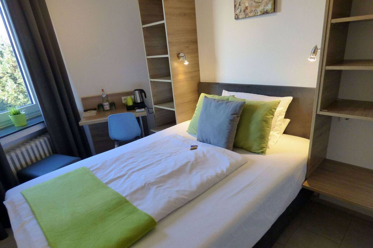 Una habitación de hotel con cama, escritorio, silla y ventana con cortinas.