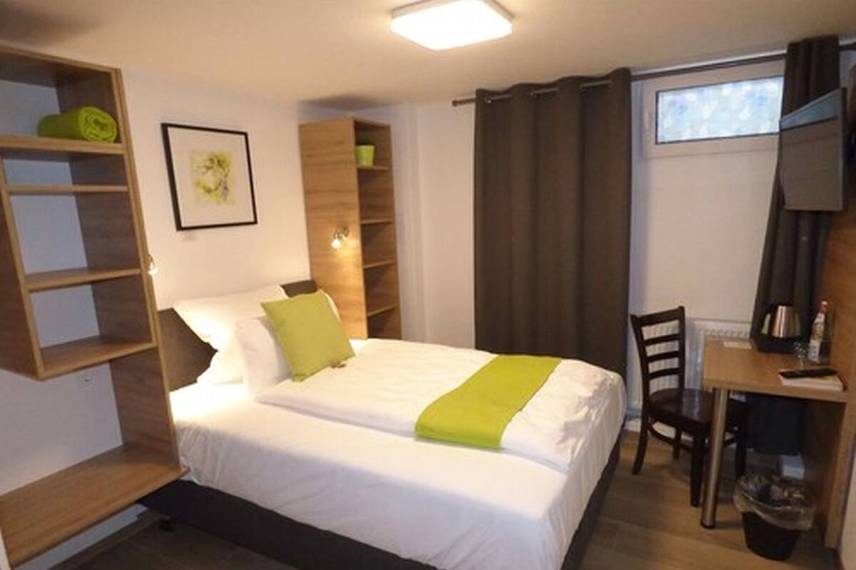 Un dormitorio con cama, escritorio y silla. Hay un estante con un objeto enrollado y un cuadro en la pared.