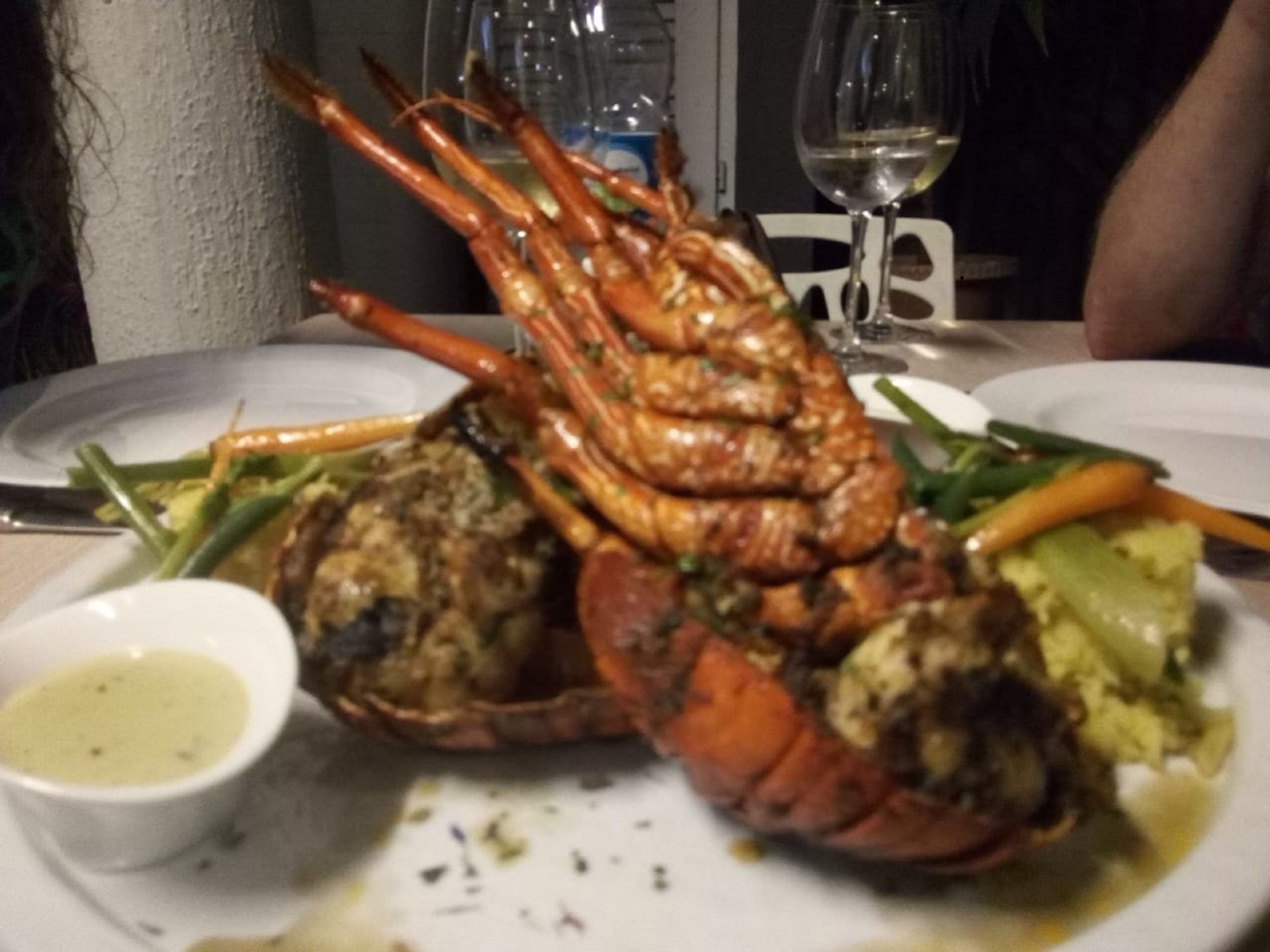 A lobster dish with vegetables and a small bowl of sauce on a plate.