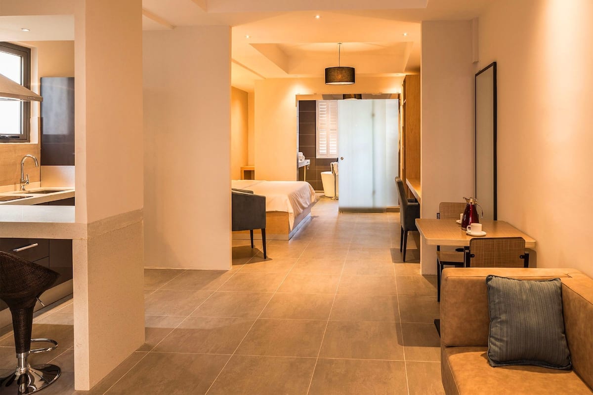 A modern hotel room with a kitchenette, a dining area, and a separate bedroom.