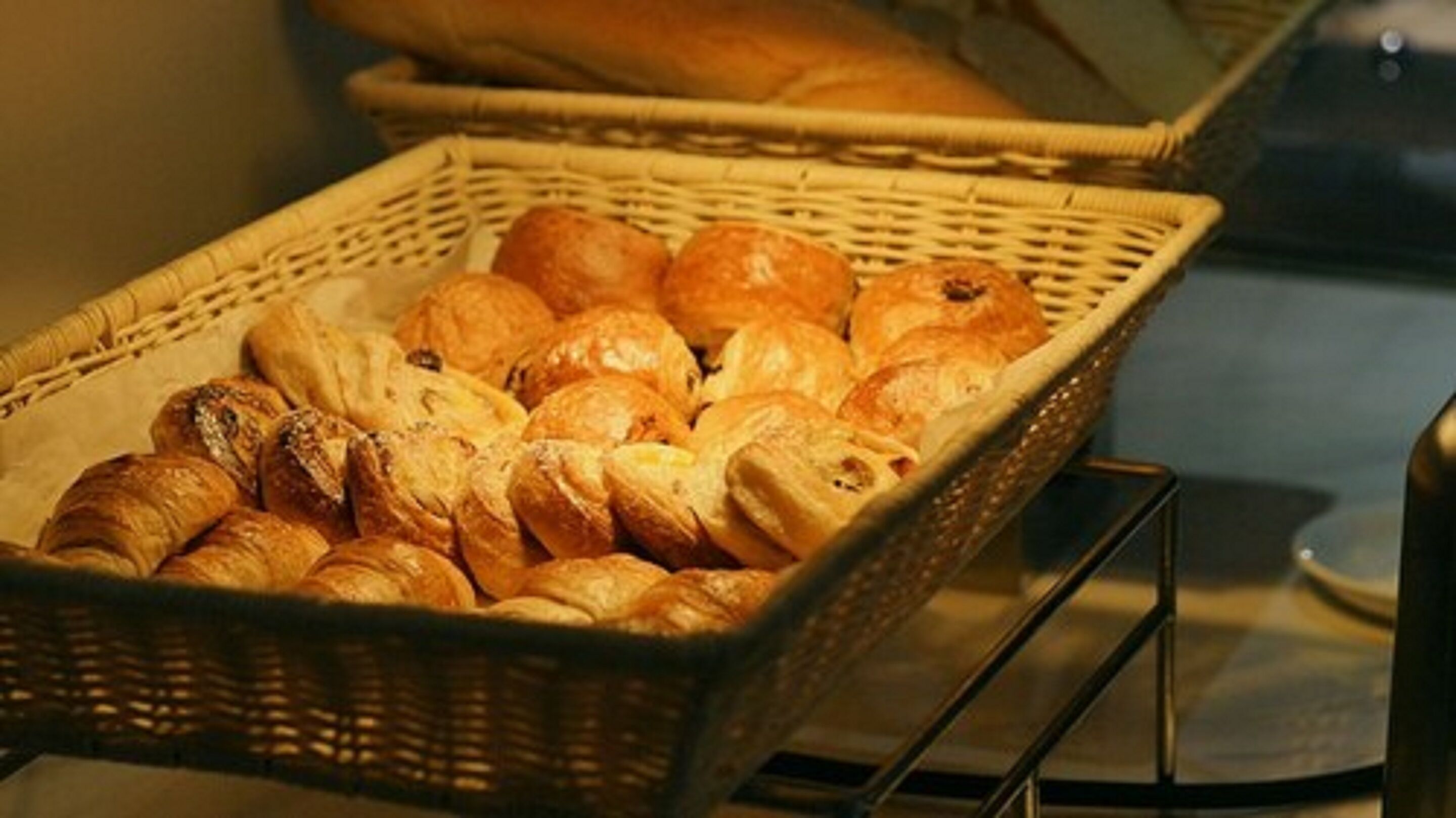 A basket filled with various types of bread, including croissants and rolls, placed on a metal stand.