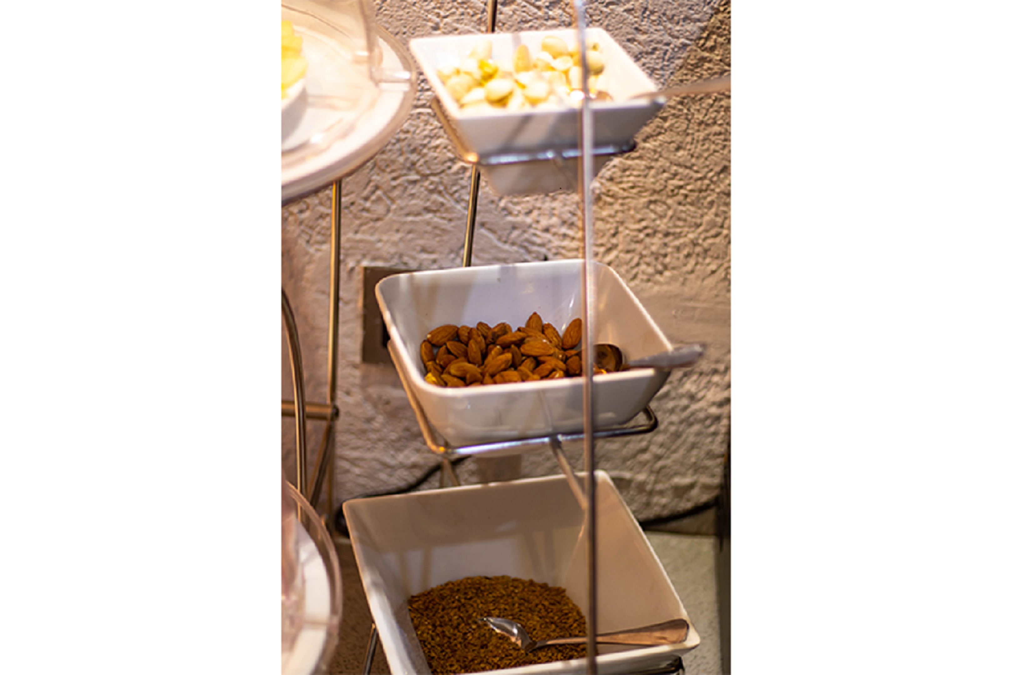Montaje de bufé con diversos alimentos en cuencos blancos sobre soportes metálicos.