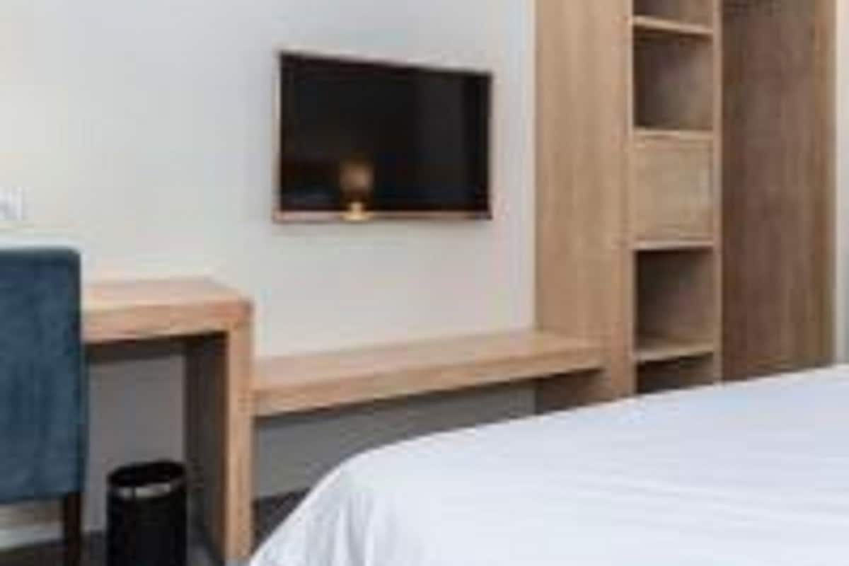 A bedroom with a bed, a desk, a chair, and a TV mounted on the wall.