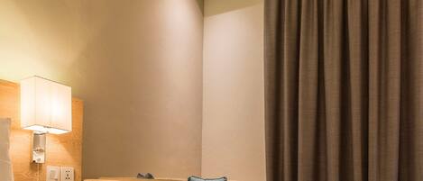 Una habitación de hotel con cama, lámpara de noche, mesita de noche y ventana con cortinas.