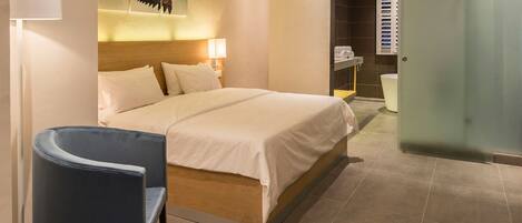 A hotel room with a bed, a chair, a painting, a bathroom, and a wardrobe.
